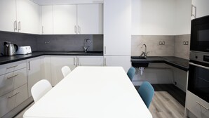 A modern kitchen with white cabinets, a black countertop, and a white dining table with blue chairs.