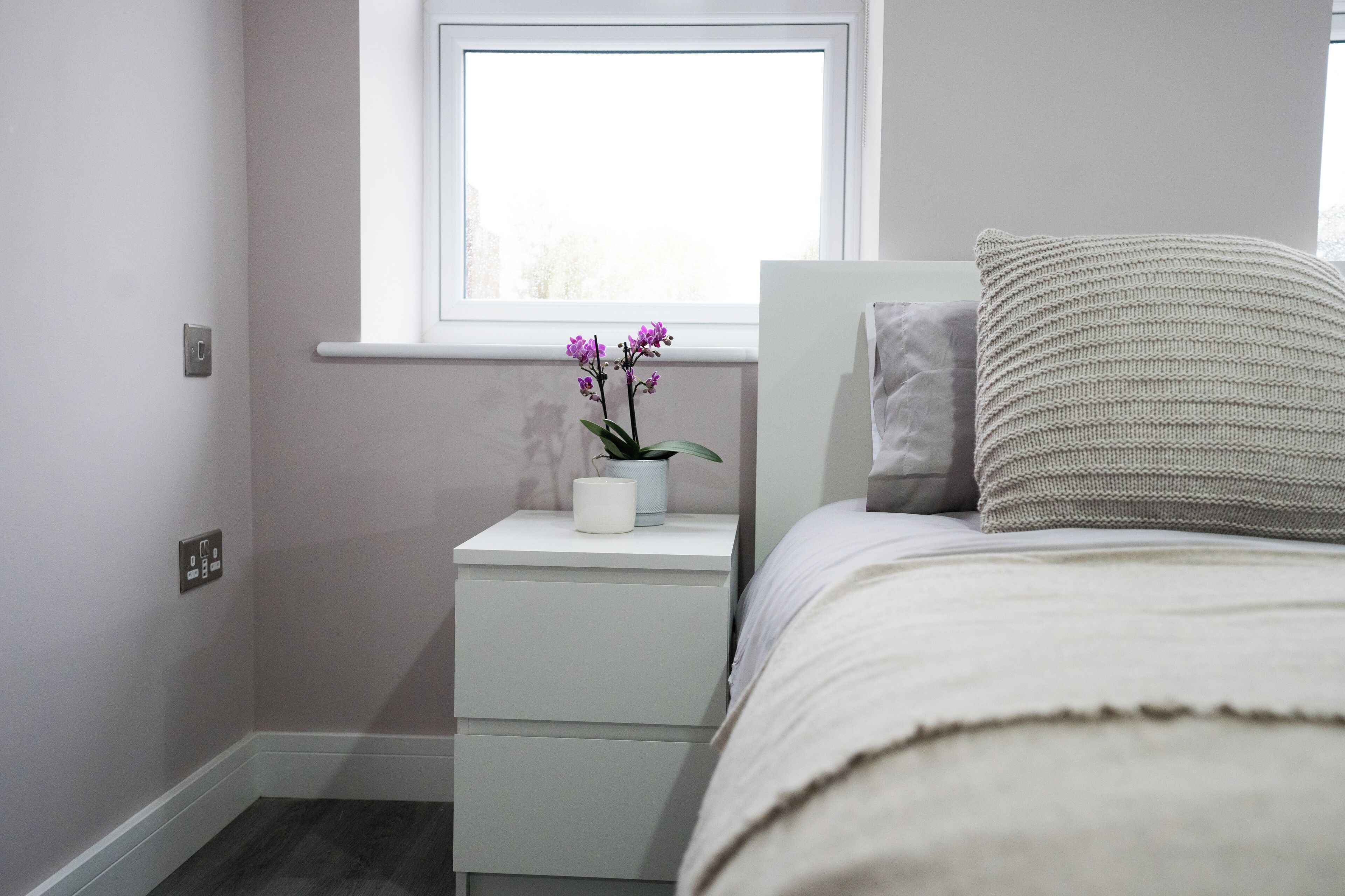 Quarto com cama, mesa de cabeceira com planta e janela com vista.