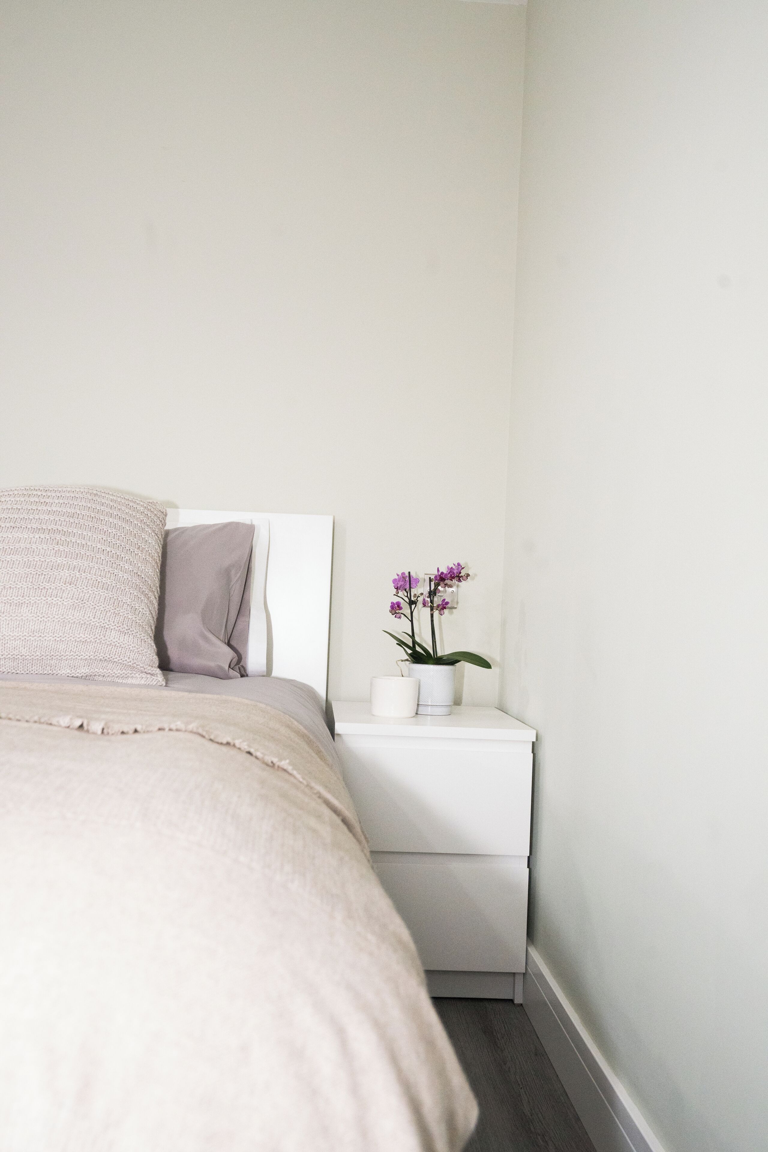 Un dormitorio con cama, almohadas, una mesita de noche y una orquídea en maceta.