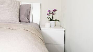 Un dormitorio con cama, almohadas, una mesita de noche y una orquídea en maceta.