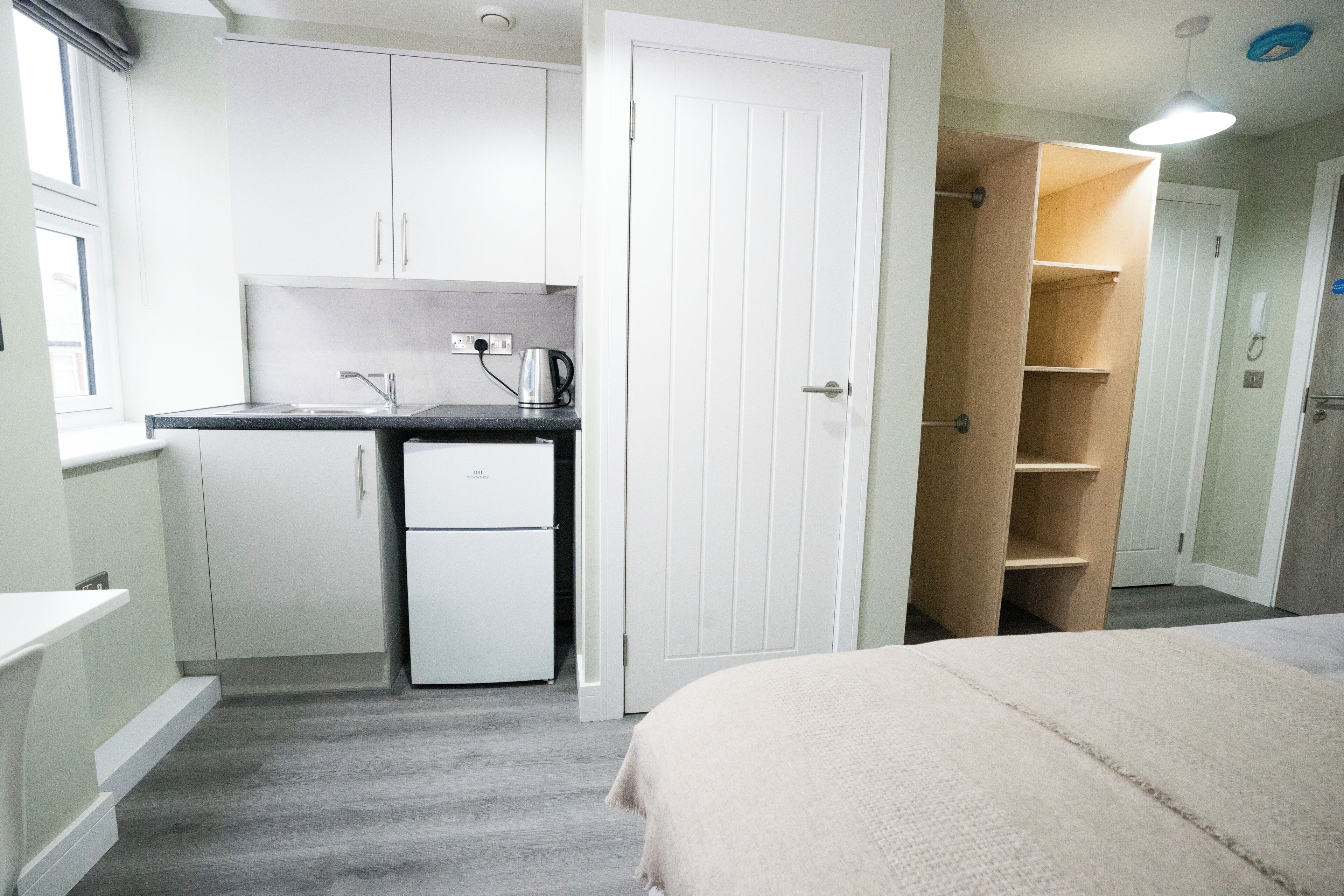 A compact room with a kitchenette, a bed, and a wardrobe.