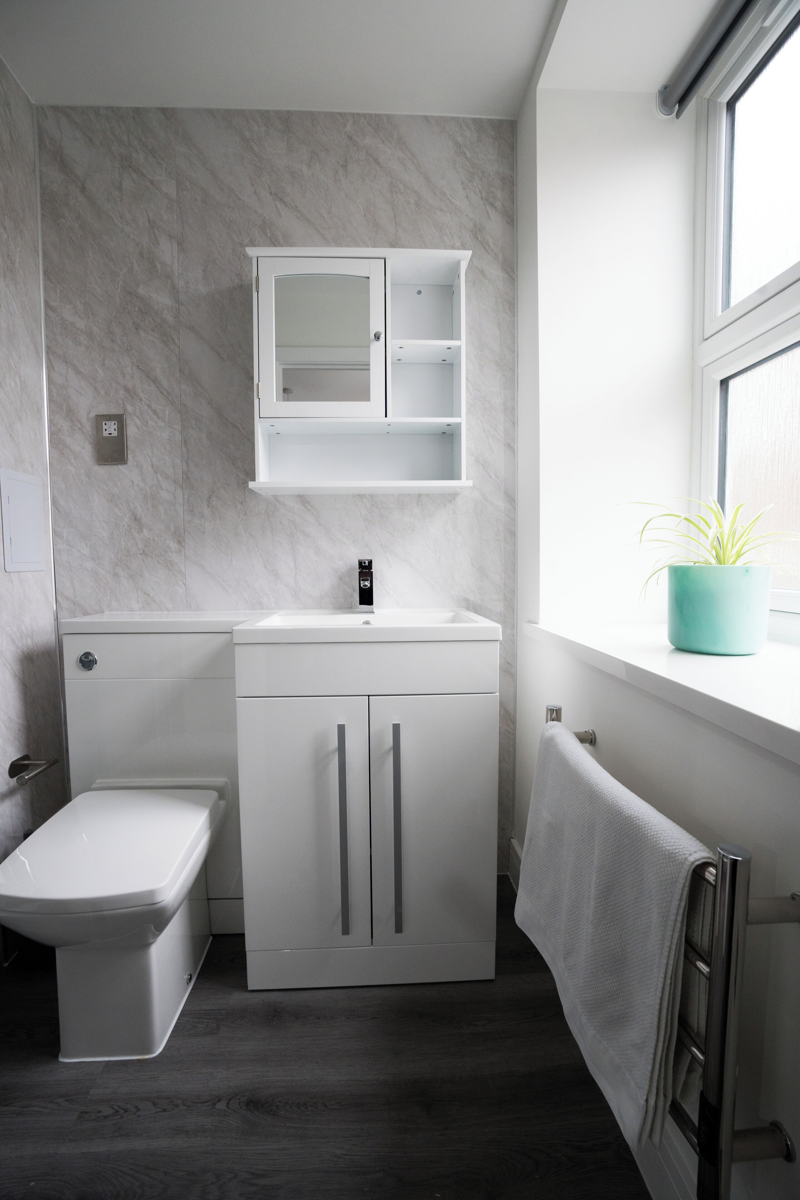Une salle de bain moderne équipée de toilettes, d’un lavabo, d’un meuble de rangement et d’une fenêtre agrémentée d’une plante.