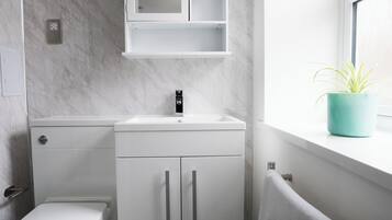 A modern bathroom with a toilet, sink, cabinet, and a window with a plant.