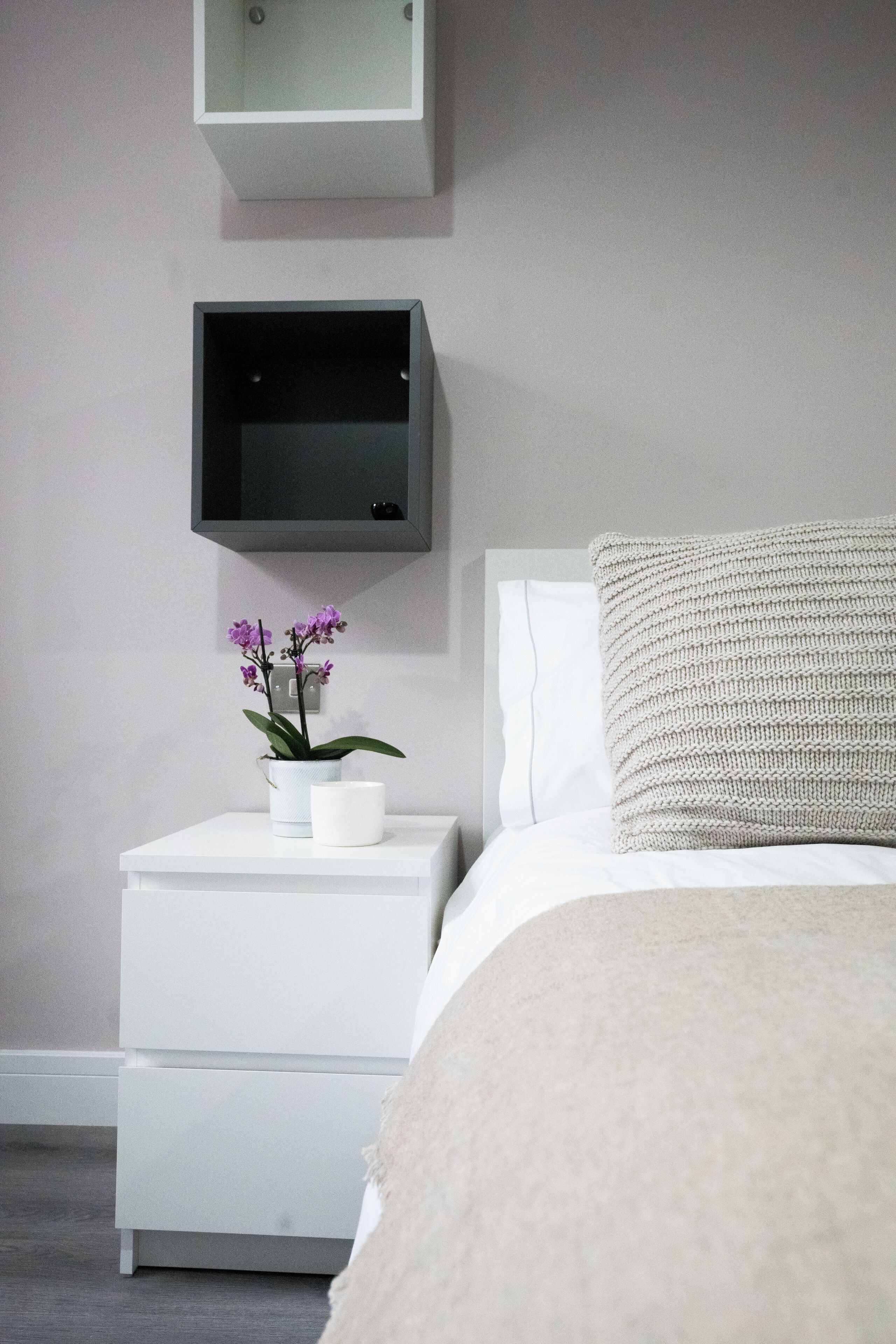 A bedroom with a bed, a nightstand with a potted orchid, a flat-screen TV, and a white dresser.