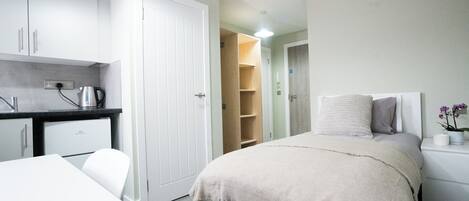 Quarto moderno com cama, mesa de cabeceira e um pequeno espaço de trabalho.