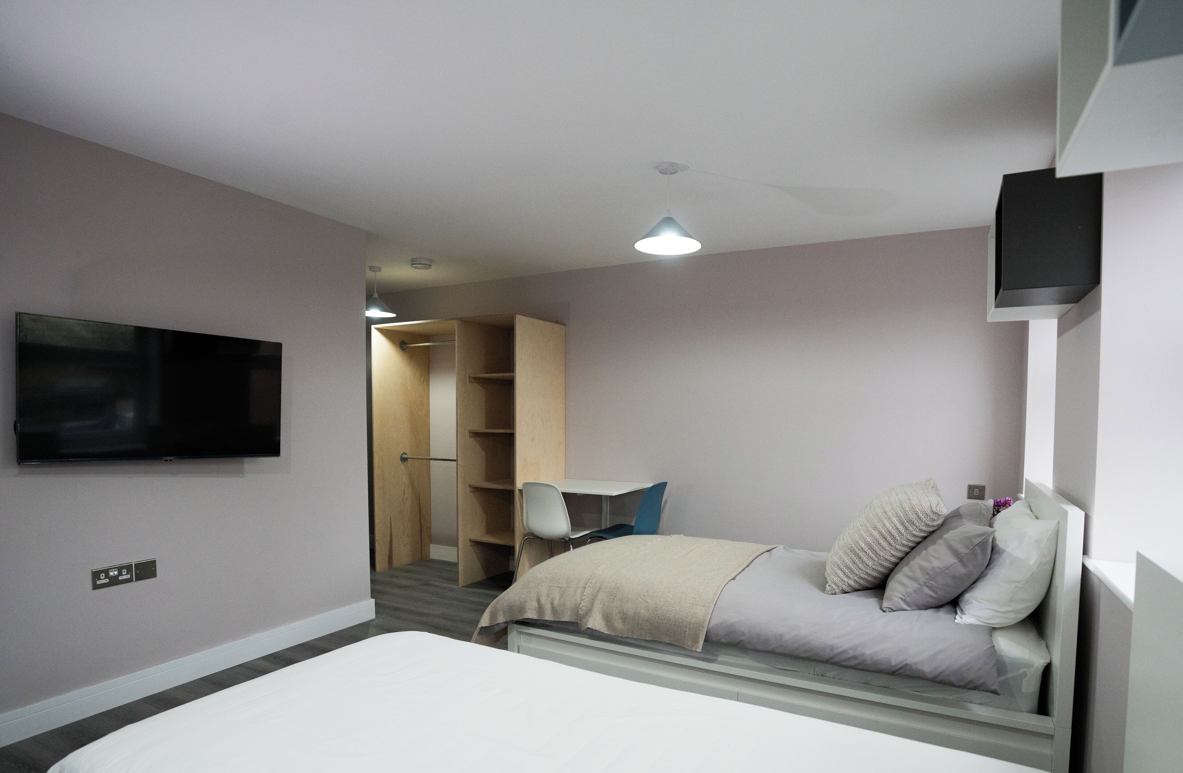 Ein Schlafzimmer mit Bett, Wandfernseher, Schreibtisch und Kleiderschrank.