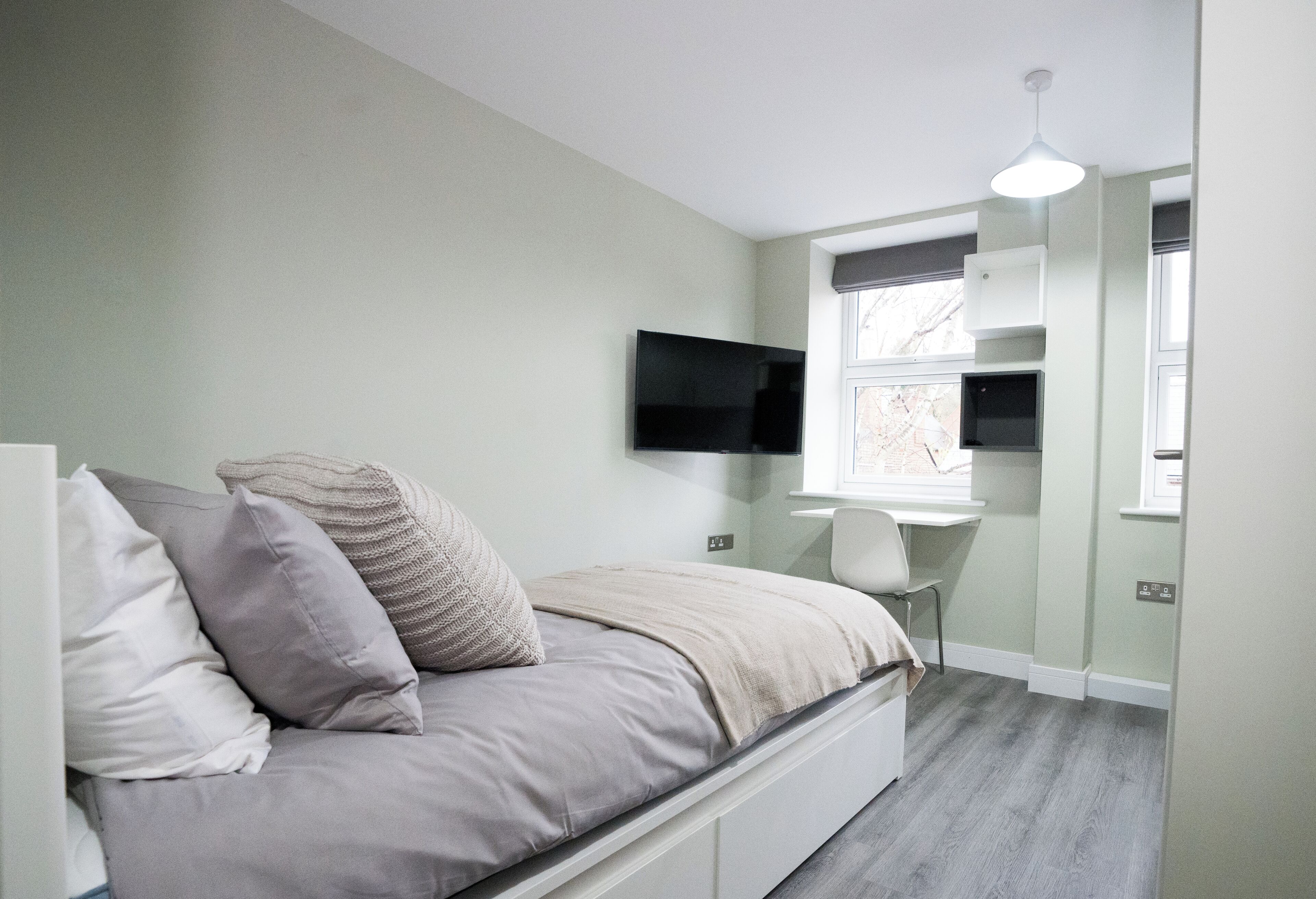 Un dormitorio con cama, televisión en la pared, escritorio y ventana.