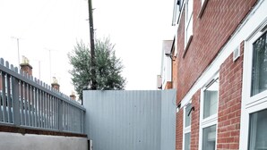 A narrow alleyway with a gravel path, bordered by a metal fence and a brick building with windows.