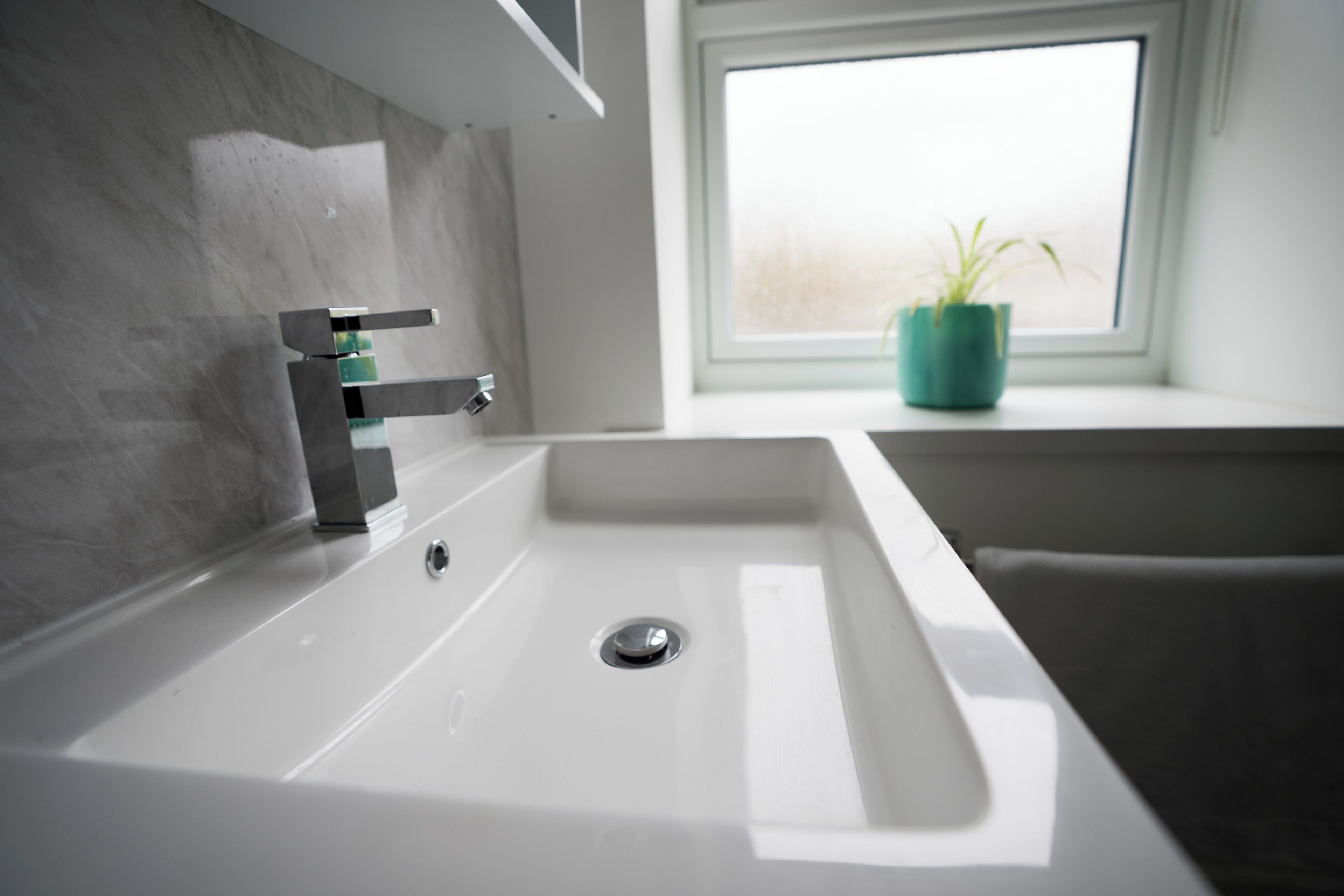 Un bagno moderno con un lavandino bianco, un rubinetto e una finestra con una pianta in vaso.