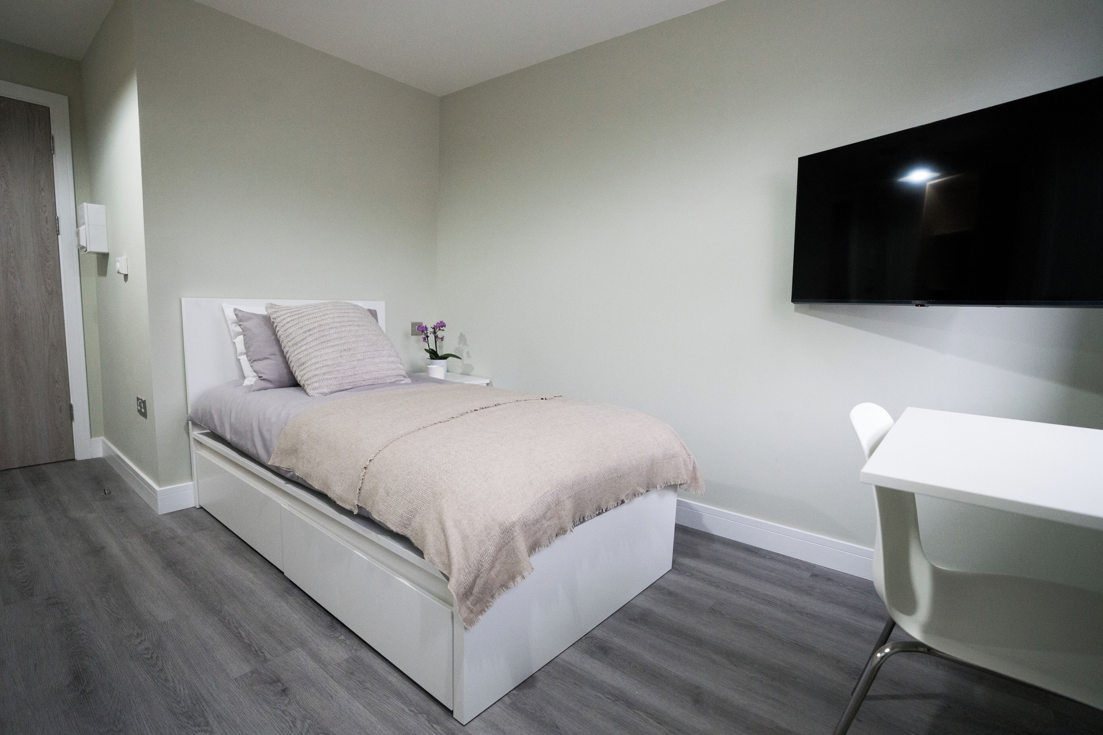 A bedroom with a bed, a desk, and a TV.
