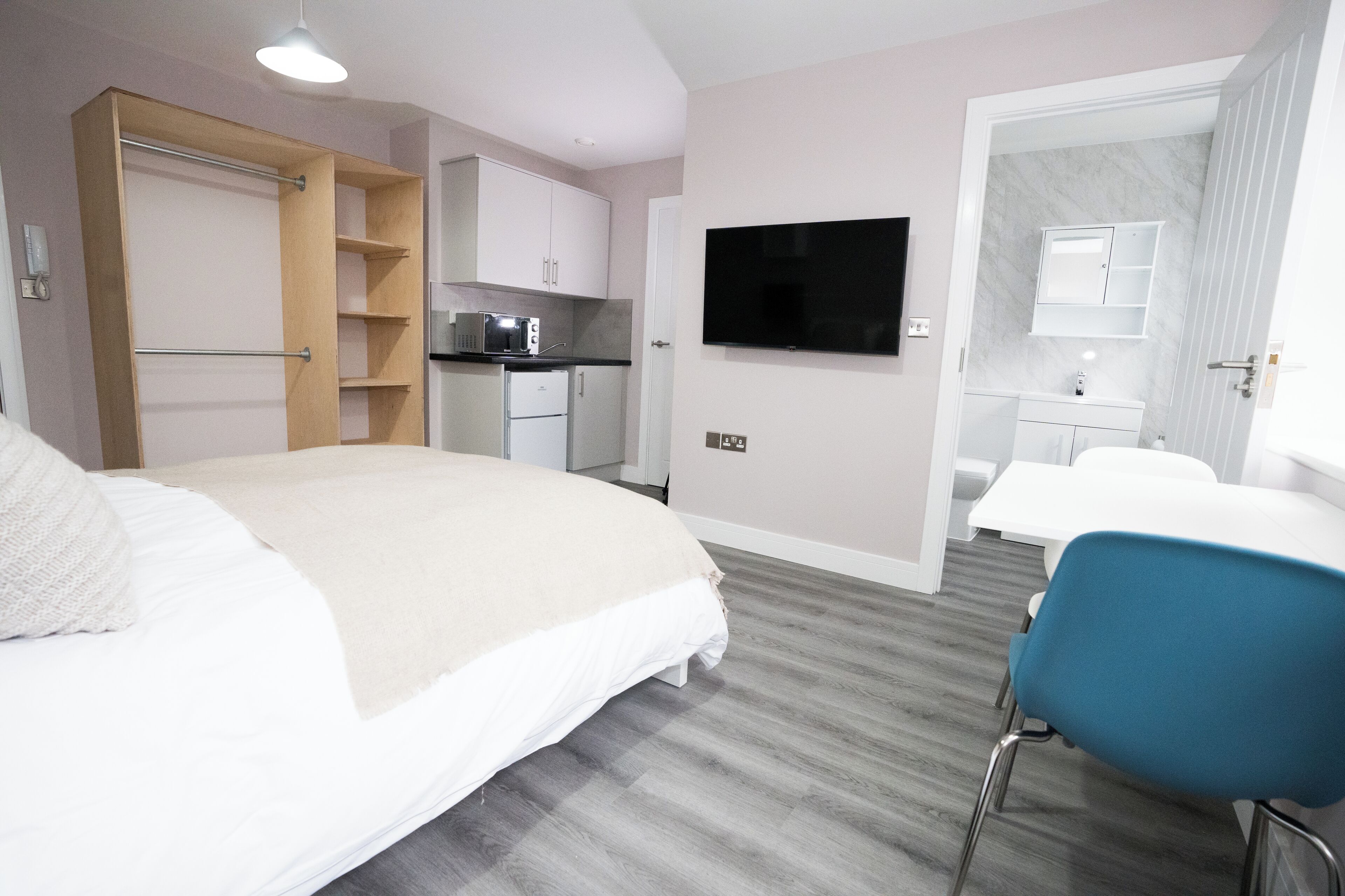 A hotel room with a bed, a desk, a chair, a TV, a kitchenette, and a bathroom.