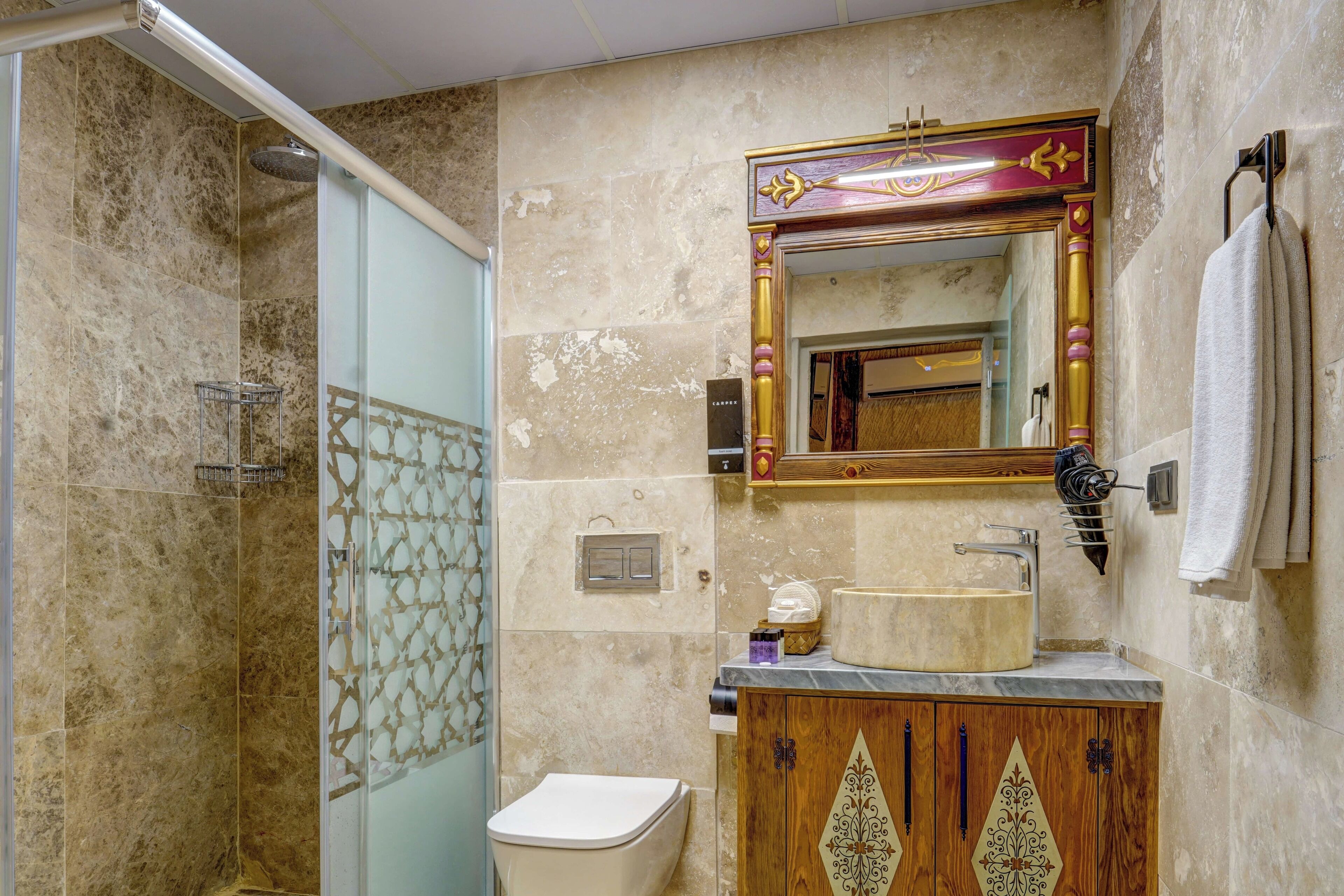 Un baño con ducha, inodoro, tocador y espejo con un marco decorativo.
