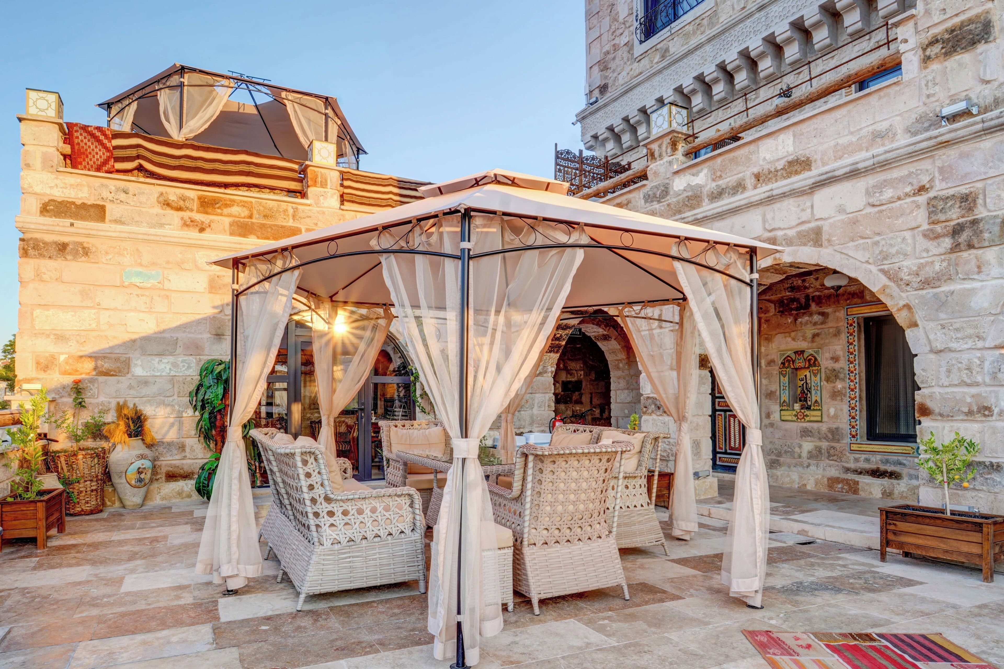 A covered outdoor seating area with wicker furniture and a canopy, set against a historic stone building.