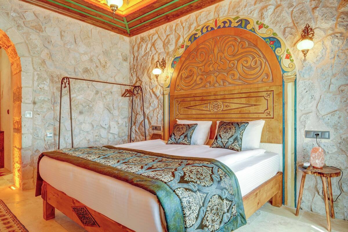 Un dormitorio con pared de piedra, una cama de madera con ropa de cama estampada y una mesita de noche con lámpara.