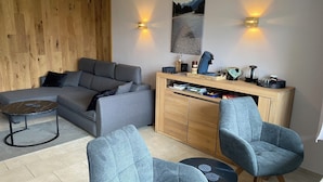 A modern living room with a grey sofa, two armchairs, a coffee table, and a wooden cabinet with books and decorative items. - FEWO in the vacation park Oberallgäu with gr. Pool, bed linen, towels, final cleaning (Missen-Wilhams)