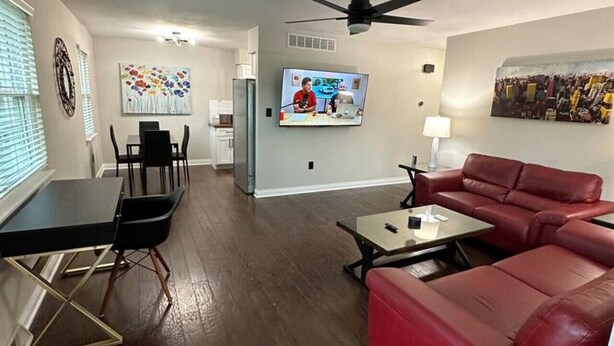 Ein modernes Wohnzimmer mit einem roten Sofa, einem Essbereich mit Tisch und Stühlen, einem an der Wand montierten Fernseher und einem Deckenventilator.