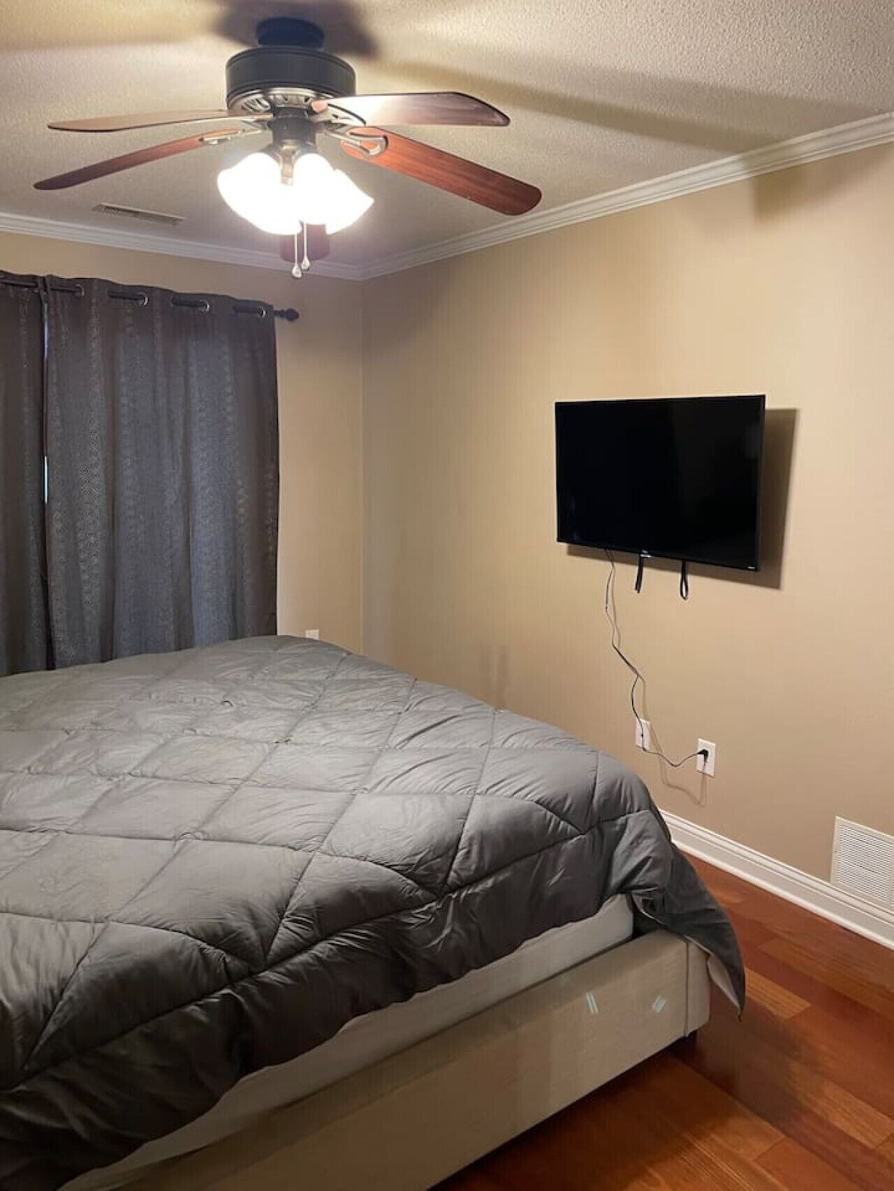 Een slaapkamer met een bed, een plafondventilator, een flatscreen televisie aan de muur en een raam met gordijnen.