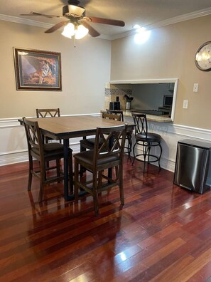 A dining area with a wooden table and chairs, a ceiling fan, a clock, and a trash can.