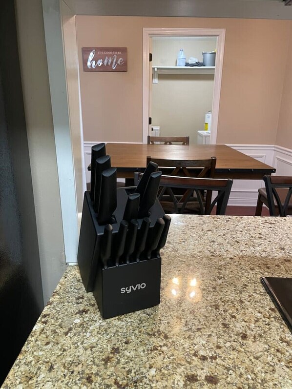 A kitchen with a granite countertop, a knife block, a dining table, and chairs.