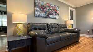 Un salon avec un canapé en cuir foncé, une table d’appoint avec une lampe et un tableau abstrait aux couleurs vives accroché au mur.