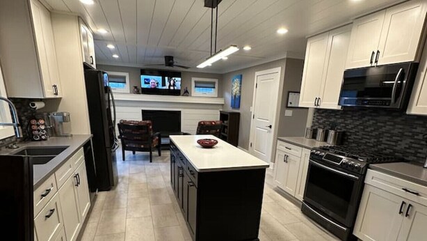Une cuisine moderne avec des meubles blancs, un îlot central et une cuisinière noire.