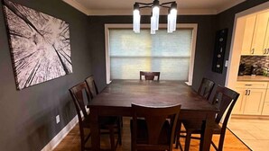 Une salle à manger avec une grande table et des chaises en bois, un lustre et un grand tableau abstrait accroché au mur.