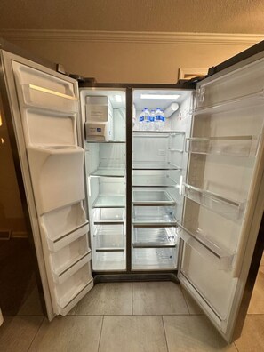 Frigorifero aperto con diversi ripiani e dispenser per acqua.
