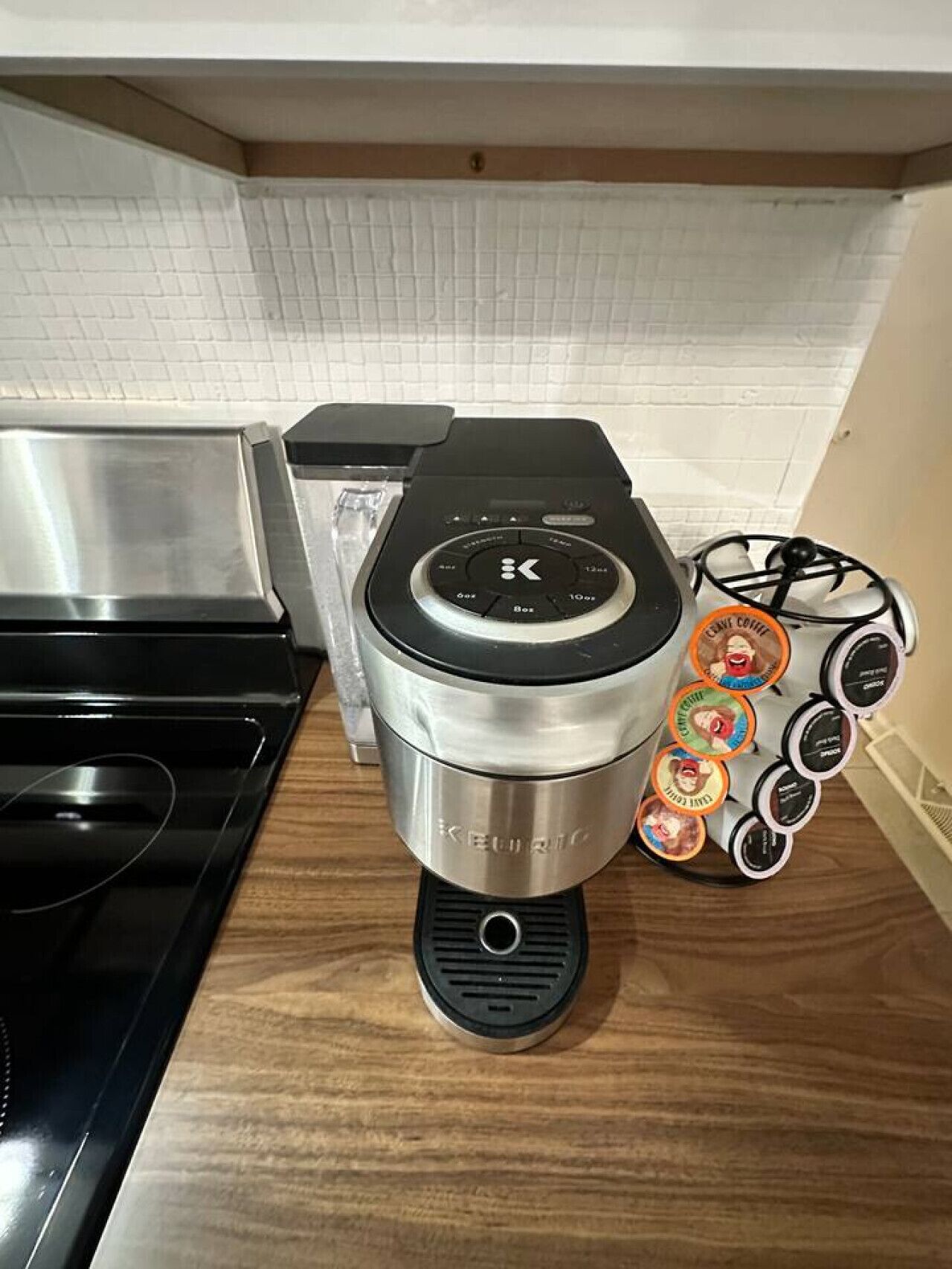 Una cafetera Keurig sobre una encimera de madera con un salpicadero blanco de azulejos y una hornilla negra.