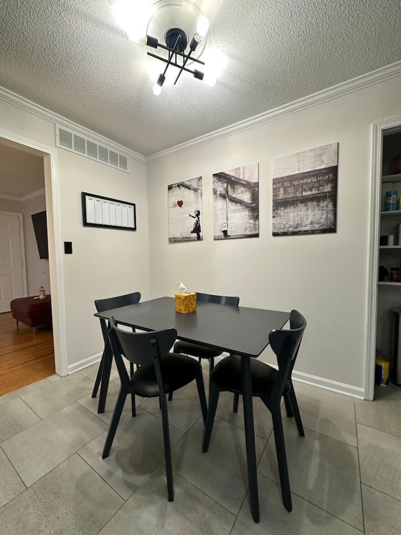 A dining area with a table and chairs, a ceiling light fixture, and three framed artworks on the wall.