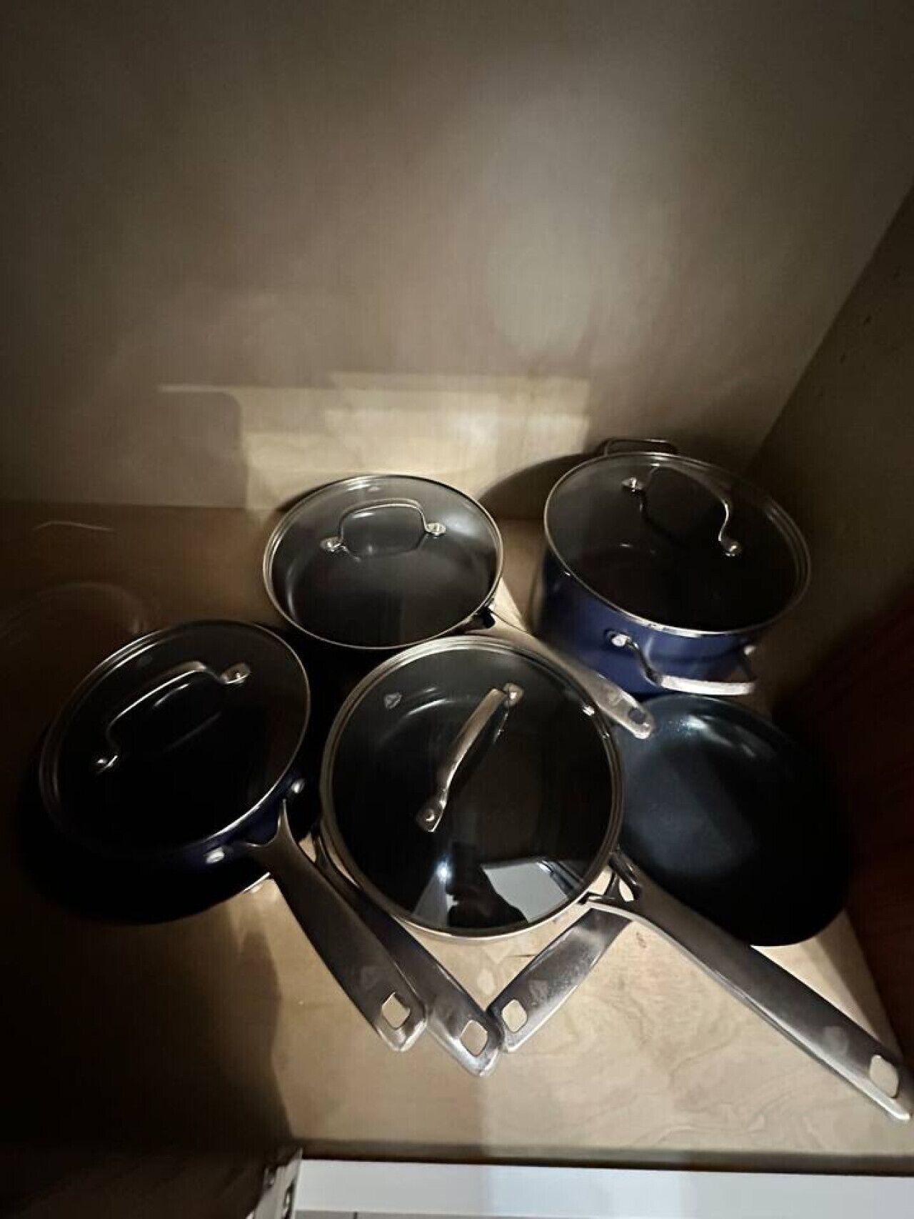 Quatre casseroles en acier inoxydable, avec leurs couvercles, posées sur une surface en bois.