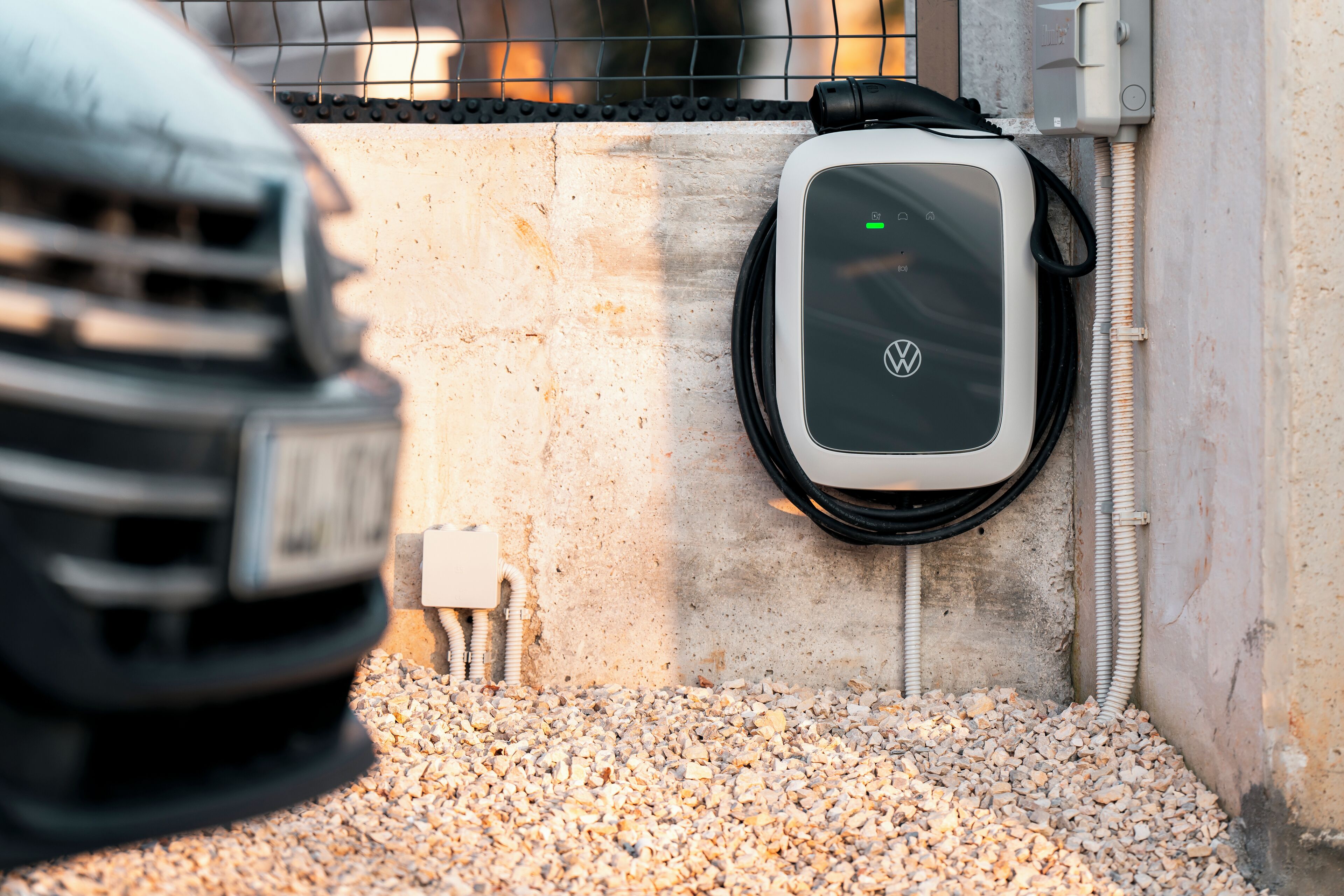 A charging station for an electric vehicle, a concrete wall, and a gravel surface.