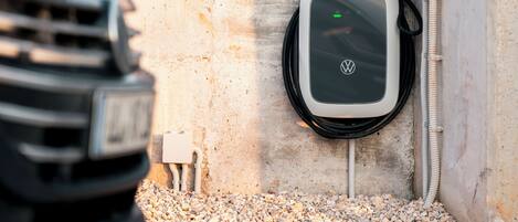 A charging station for an electric vehicle, a concrete wall, and a gravel surface.