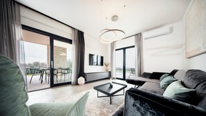 A modern living room with a sofa, armchair, and coffee table. There is a TV mounted on the wall and a large window with curtains. - Villa SUN Villa with pool and sea view (Labinci)
