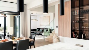 A modern dining area with a table set for two, a sofa, and a bookshelf in the background. - Villa SUN Villa with pool and sea view (Labinci)