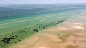 Vista aérea de una zona costera con aguas cristalinas, playas de arena y un barco visible.