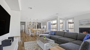 Una sala de estar moderna con un sofá gris, una mesa de centro y un televisor. Hay una zona de cocina con una mesa de comedor y sillas.