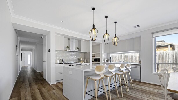 Una cocina moderna con armarios blancos, una isla central con taburetes altos e iluminación colgante.