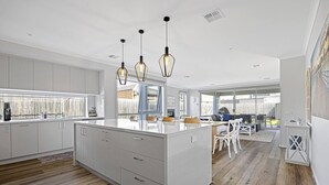 Una cocina moderna con armarios blancos, una isla grande, iluminación colgante y vistas al patio trasero.
