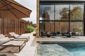 A modern outdoor pool area with lounge chairs and a large umbrella. - Pousada Maria do Mar (Fernando de Noronha)