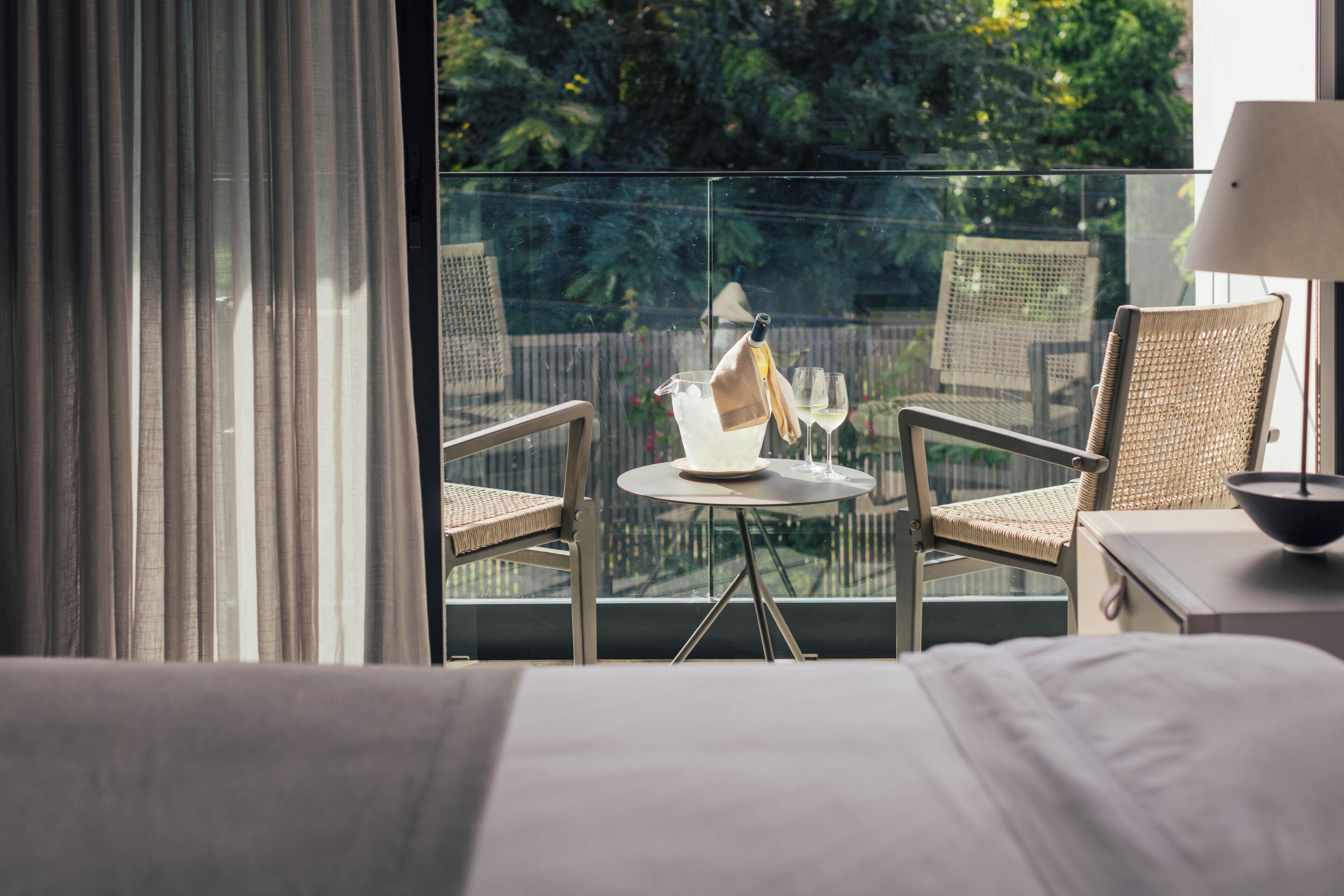 A balcony with a table, two wicker chairs, a bottle, and a glass.