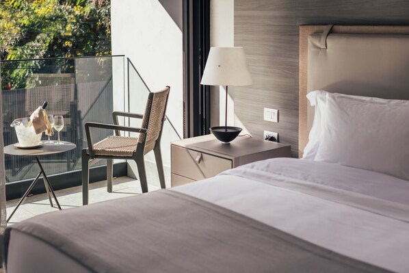 Une chambre d’hôtel avec un lit, une chaise, une petite table avec une bouteille et des verres, une lampe et une vue sur la verdure à l’extérieur.