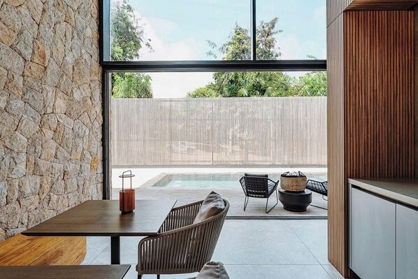 A modern interior with a stone wall, a wooden table, and a seating area with a view of a fenced outdoor space. - Pousada Maria do Mar (Fernando de Noronha)