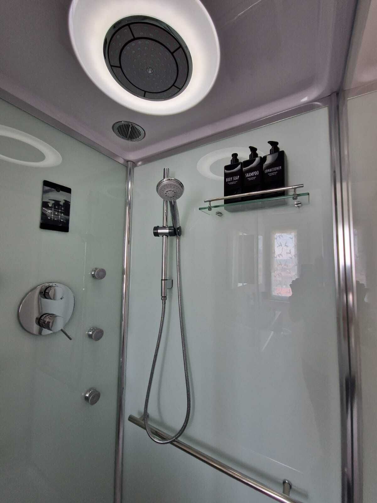 A modern shower with a handheld showerhead, a wall-mounted control panel, and a glass shelf with toiletries.
