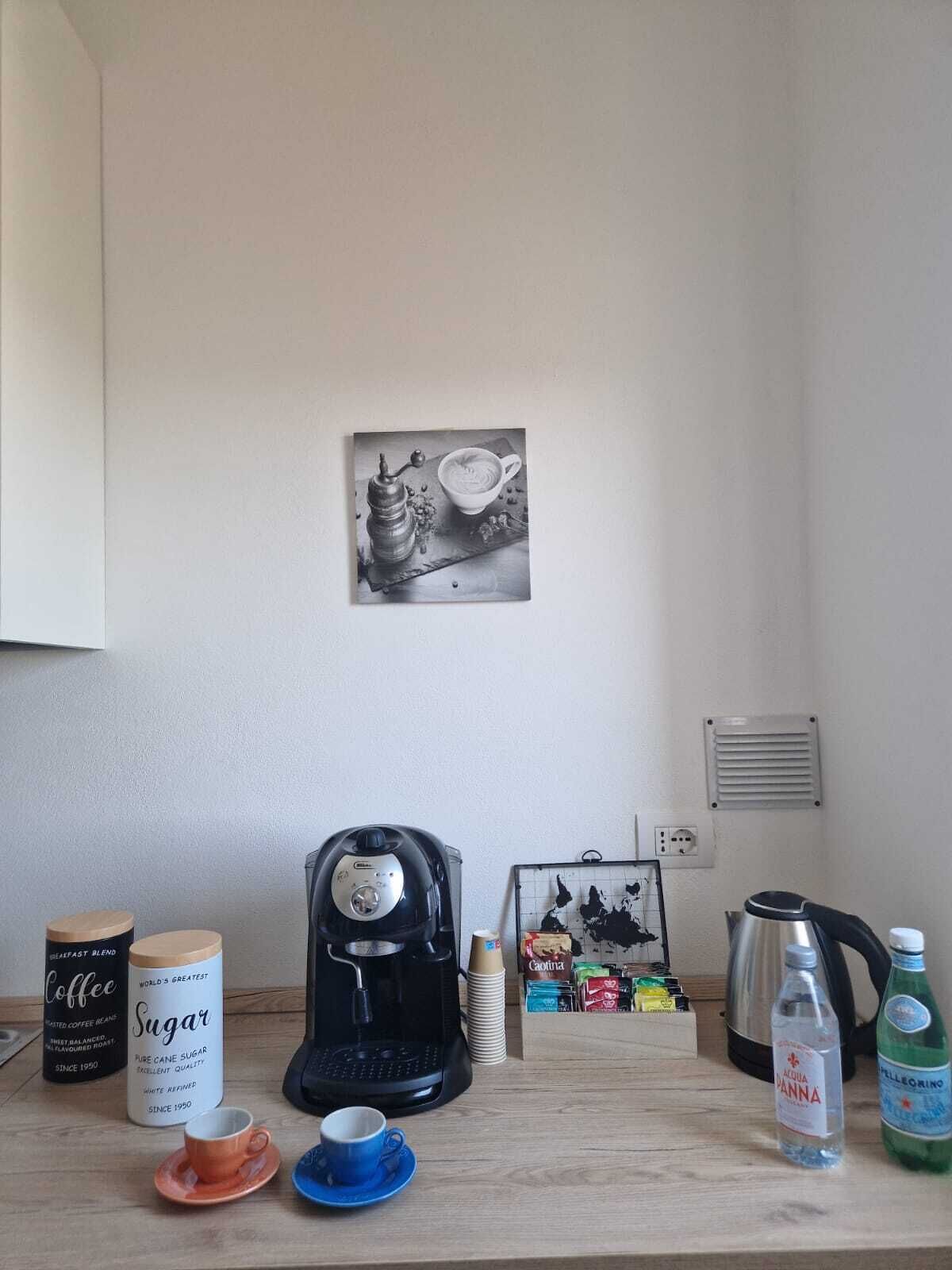 A kitchen counter with a coffee maker, a coffee jar, a sugar container, a coffee cup, a stack of coffee cups, a water bottle, and a bottle of water.