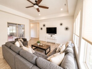 A modern living room with a sectional sofa, a coffee table, a TV, and a ceiling fan.
