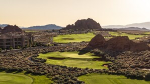 Un parcours de golf avec des bunkers, un bâtiment et une chaîne de montagnes en arrière-plan.