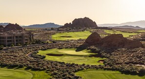 Un campo de golf con búnkeres, un edificio y montañas al fondo.