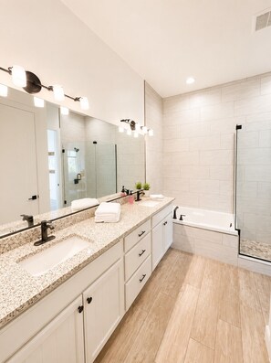 Un baño moderno con un espejo grande, dos lavamanos, una bañera y una ducha.