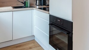 Een moderne keuken met witte kasten, een houten spatwand, een zwarte oven en een hangende hanglamp.