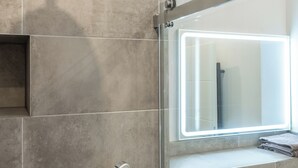 Een moderne badkamer met een douchecabine van glas, een ingebouwde handdoekhouder en een wandbevestigde zeepdispenser.